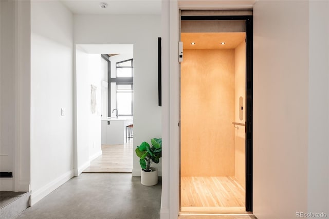 hallway featuring elevator, sink, and concrete flooring