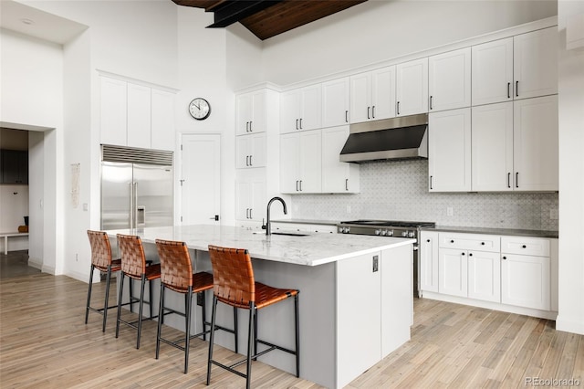 kitchen featuring sink, white cabinets, a high ceiling, beam ceiling, and a center island with sink