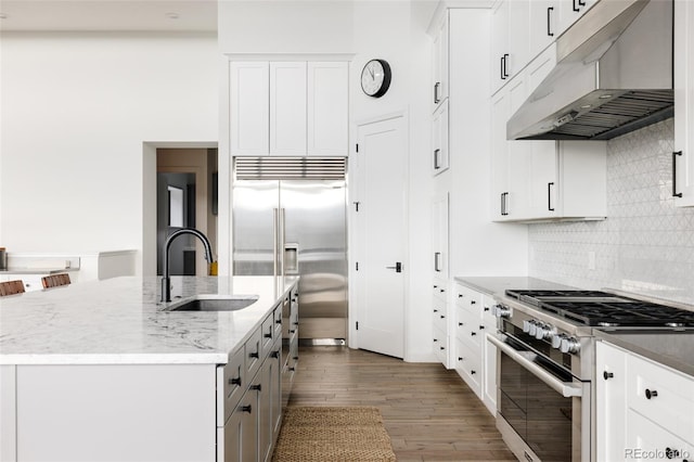 kitchen with sink, high end appliances, a kitchen island with sink, and white cabinetry