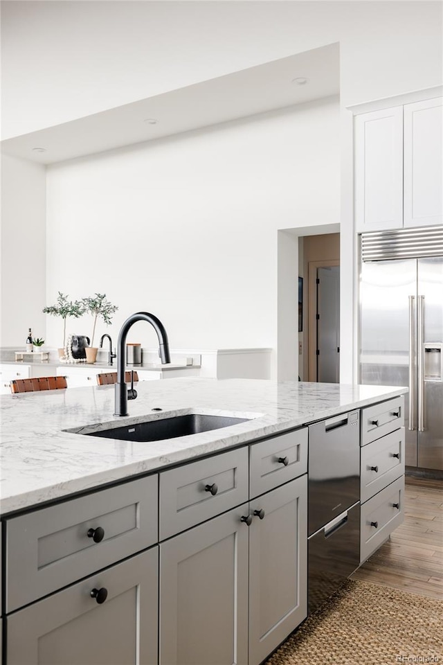 kitchen featuring light stone countertops, gray cabinetry, sink, light wood-type flooring, and stainless steel built in refrigerator