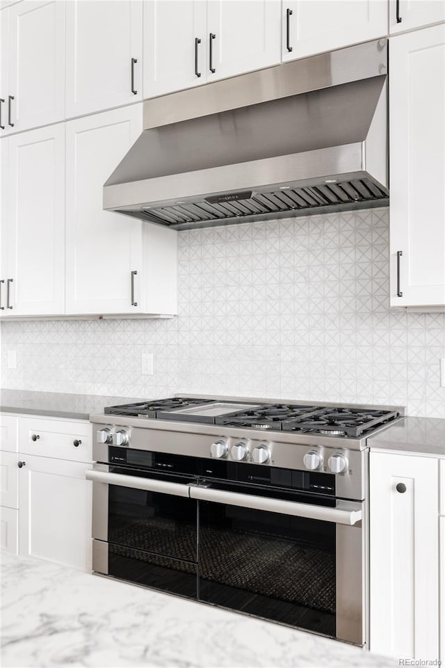 kitchen featuring stainless steel range with gas cooktop, white cabinets, ventilation hood, and tasteful backsplash