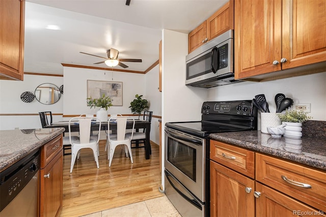 kitchen featuring stainless steel appliances, ceiling fan, crown molding, light tile patterned floors, and dark stone countertops