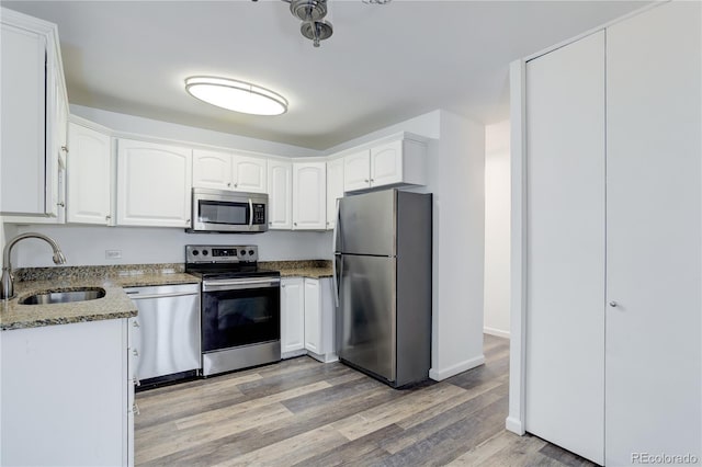 kitchen with stainless steel appliances, a sink, stone countertops, light wood finished floors, and white cabinetry