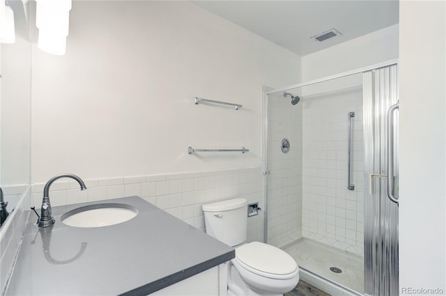 full bath featuring vanity, tile walls, a shower stall, toilet, and a wainscoted wall