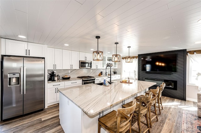 kitchen with white cabinets, light stone counters, wood finished floors, and appliances with stainless steel finishes