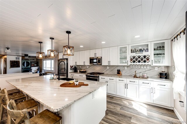 kitchen featuring light stone countertops, a sink, decorative backsplash, appliances with stainless steel finishes, and a kitchen breakfast bar