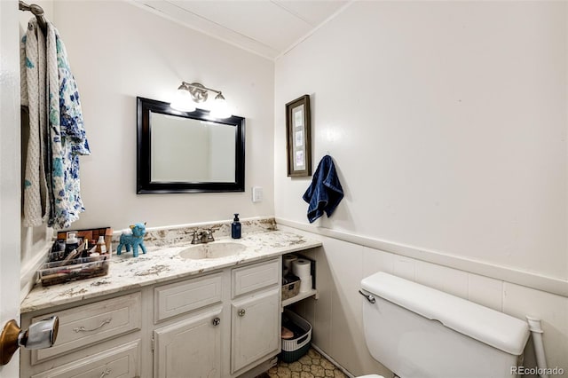 bathroom with a wainscoted wall, toilet, vanity, and crown molding