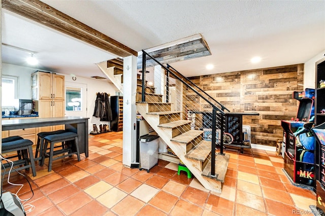 staircase featuring tile patterned floors, beamed ceiling, wooden walls, and a textured ceiling