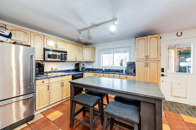 kitchen featuring a sink, light brown cabinetry, stainless steel appliances, a textured ceiling, and dark countertops