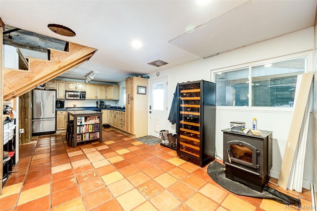 kitchen with beverage cooler, a kitchen island, dark countertops, stainless steel appliances, and a wood stove