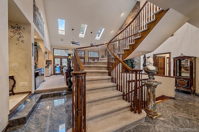 stairs featuring ceiling fan, a skylight, carpet, and a towering ceiling