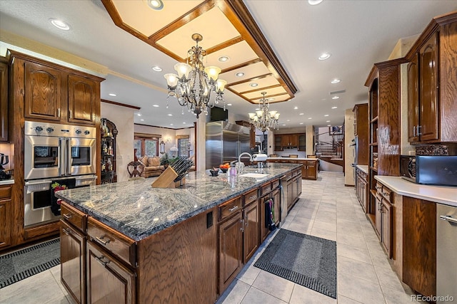 kitchen with a notable chandelier, light tile floors, appliances with stainless steel finishes, hanging light fixtures, and a kitchen island with sink