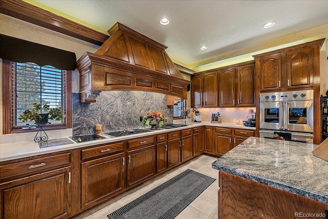 kitchen with double oven, light tile flooring, premium range hood, black electric stovetop, and tasteful backsplash