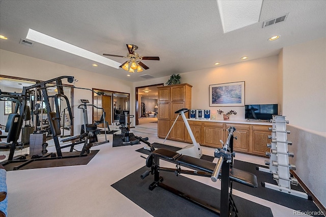 exercise area featuring light carpet, a textured ceiling, ceiling fan, and a skylight