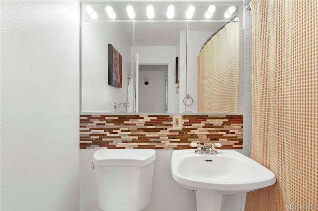 bathroom featuring backsplash, toilet, tile walls, and a sink