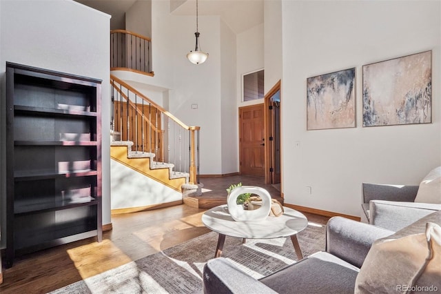 living room featuring a high ceiling, stairway, baseboards, and wood finished floors