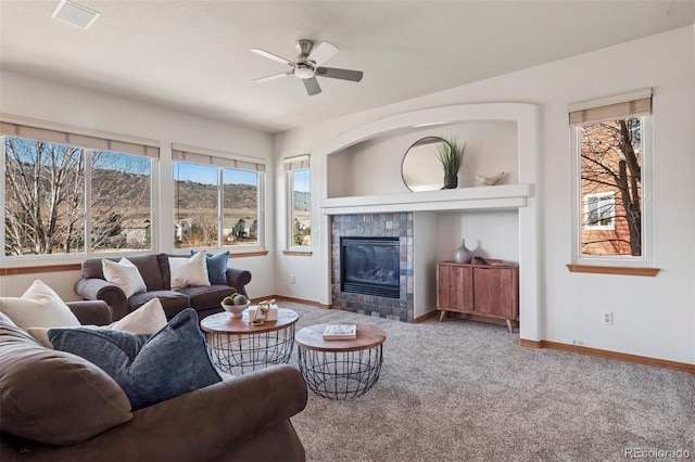 living area with ceiling fan, a tiled fireplace, baseboards, and carpet flooring