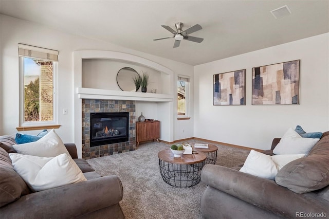 carpeted living area with baseboards, a ceiling fan, a wealth of natural light, and a tile fireplace