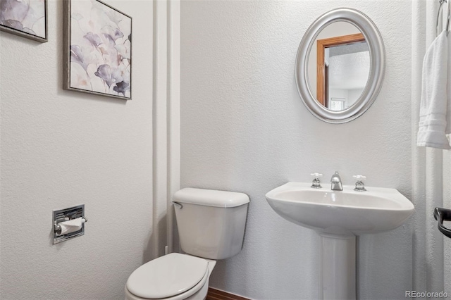 bathroom featuring toilet, a sink, and a textured wall