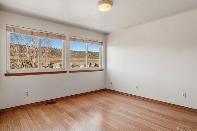 spare room featuring light wood finished floors, visible vents, and baseboards