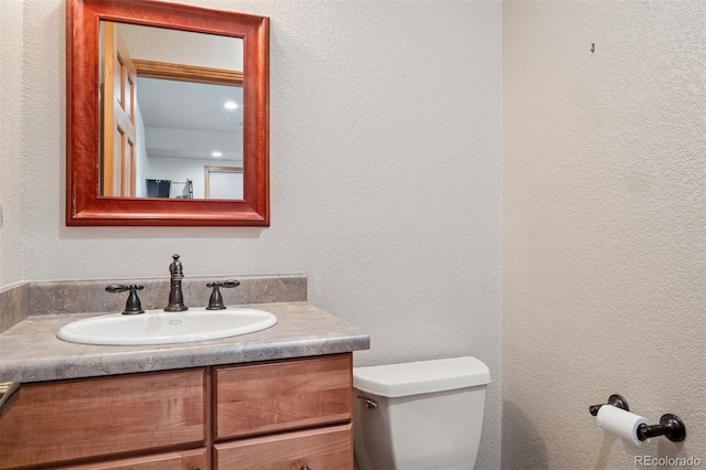 half bath with toilet, a textured wall, and vanity