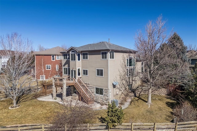 rear view of property featuring central AC unit, stone siding, stairs, fence, and a yard