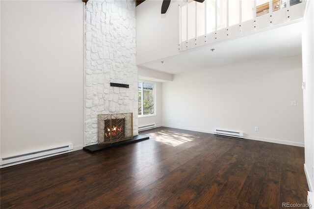 4062 S Atchison Way Unit 302, Aurora, CO 80014 - unfurnished living room featuring a baseboard heating unit, wood finished floors, a ceiling fan, a stone fireplace, and a towering ceiling