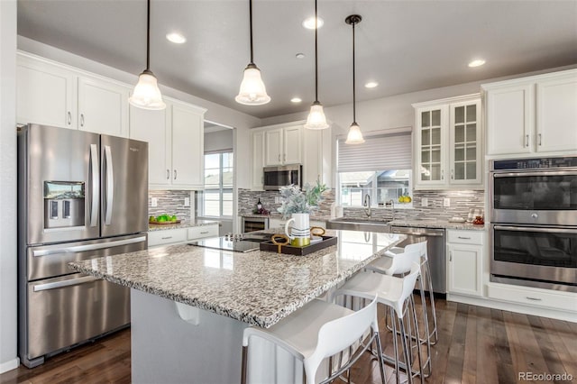 kitchen with a kitchen island, white cabinets, hanging light fixtures, appliances with stainless steel finishes, and glass insert cabinets