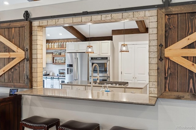 kitchen with appliances with stainless steel finishes, beamed ceiling, decorative light fixtures, white cabinetry, and a barn door