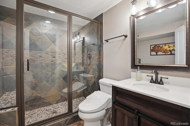 full bath with a textured wall, toilet, vanity, and a shower stall