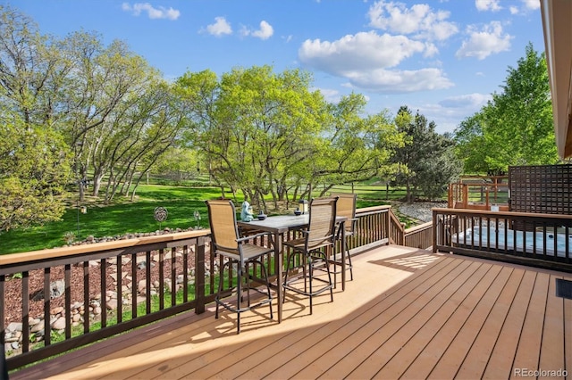 wooden terrace with outdoor dining area, a yard, and view of wooded area