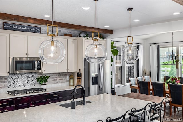 kitchen featuring hanging light fixtures, decorative backsplash, appliances with stainless steel finishes, white cabinets, and a sink