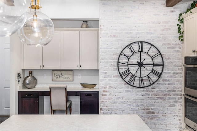 kitchen with stainless steel double oven, brick wall, white cabinetry, light countertops, and built in study area