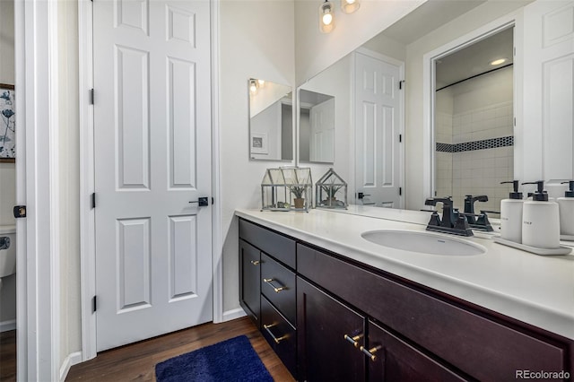 bathroom with baseboards, tiled shower, wood finished floors, and vanity