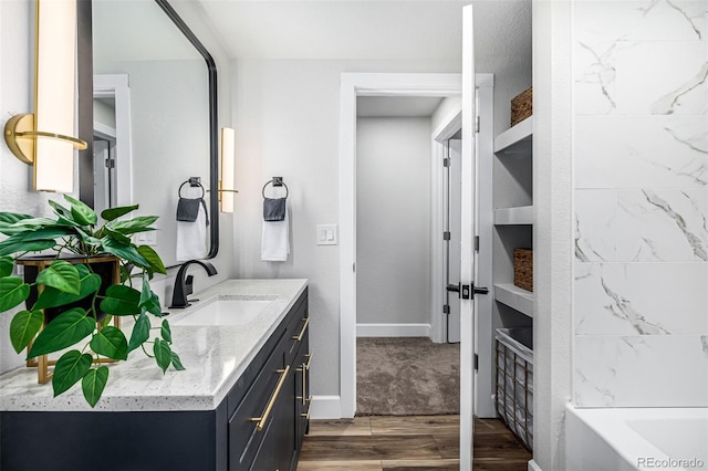 full bathroom with a tub to relax in, vanity, baseboards, and wood finished floors