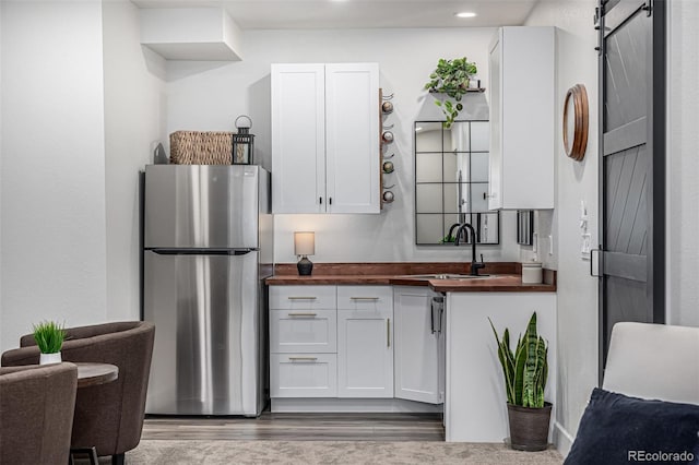 kitchen with a barn door, freestanding refrigerator, white cabinetry, wooden counters, and a sink