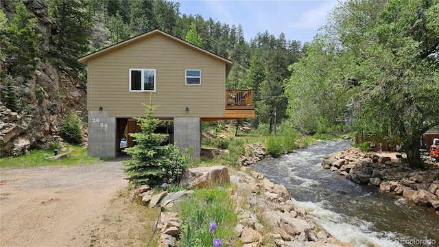 view of side of home with dirt driveway, a deck, and a view of trees