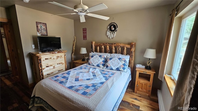 bedroom with a ceiling fan, baseboard heating, and wood finished floors