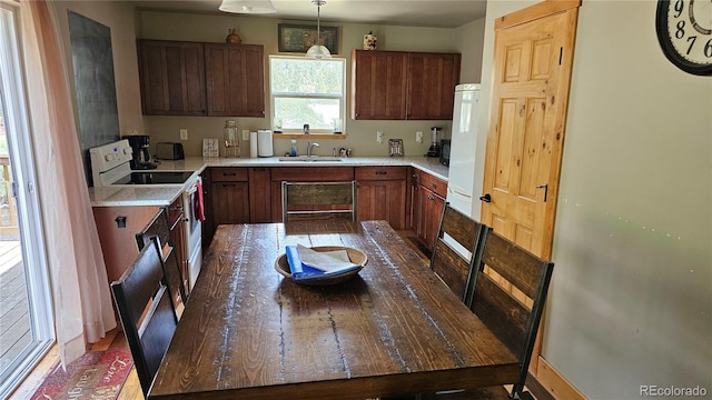 kitchen with hanging light fixtures, white range with electric cooktop, light countertops, and a sink