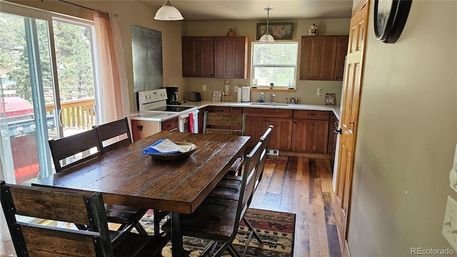 kitchen with white range with electric stovetop, light countertops, hanging light fixtures, a sink, and hardwood / wood-style floors