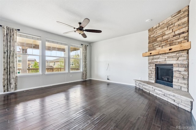 unfurnished living room with a stone fireplace, dark wood finished floors, ceiling fan, and baseboards