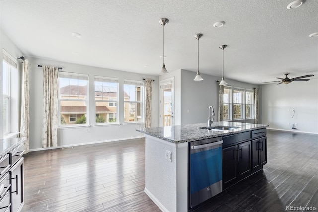 kitchen with dark wood finished floors, dishwasher, a sink, light stone counters, and open floor plan