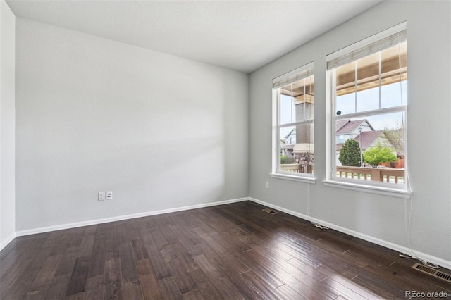 empty room featuring dark wood-style flooring, baseboards, and visible vents