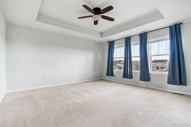 carpeted empty room with a raised ceiling, baseboards, a ceiling fan, and visible vents