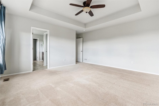 empty room with light colored carpet, ceiling fan, visible vents, and a raised ceiling