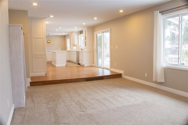 unfurnished living room featuring sink, plenty of natural light, and light colored carpet