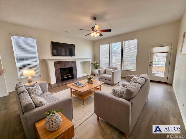 living room featuring ceiling fan, a fireplace, baseboards, and wood finished floors