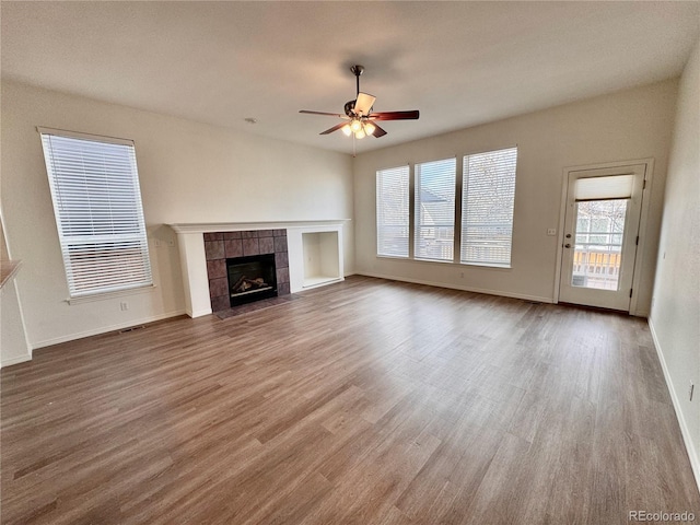 unfurnished living room with visible vents, a ceiling fan, wood finished floors, a tile fireplace, and baseboards