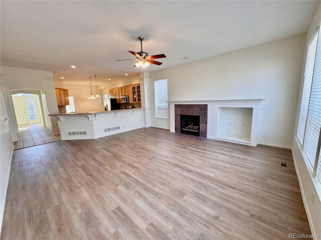 unfurnished living room featuring light wood-type flooring, visible vents, ceiling fan, and a tile fireplace