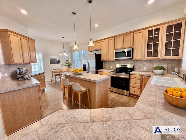 kitchen featuring stainless steel appliances, a sink, a center island, a kitchen bar, and glass insert cabinets